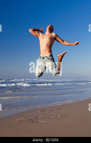 Jeune homme sautant sur la plage Banque D'Images