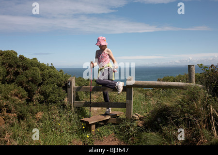 Une fillette de onze ans précairement étapes sur une stile sur le sentier du littoral à Carregwastad Point. Banque D'Images