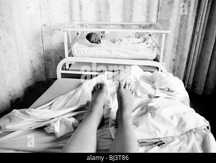 Une petite fille nouveau-né dort dans son lit au pied du lit de sa mère dans une maternité d'un hôpital. Banque D'Images