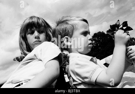 Une grande sœur se retourne pour voir ce que son plus jeune frère est jusqu'à qu'elles s'asseoir dos à dos dans un parc de Londres de l'été. Banque D'Images