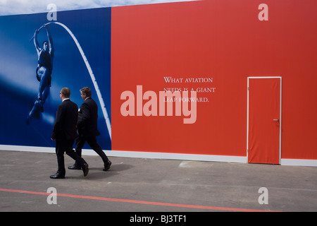 Deux hommes d'affaires passent par un slogan sur l'avenir de l'industrie de l'aviation écrit sur un panneau publicitaire rouge à Farnborough Air Show Banque D'Images