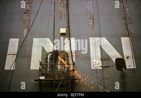 Avec des étincelles orange avalée ci-dessous, un constructeur de soudures en se tenant sur le bras d'échafaudage sur coque de grand ferry allemand. Banque D'Images