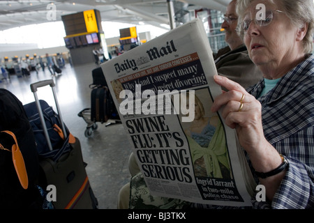 Deux personnes âgées mais billet-sage passagers lire le journal Daily Mail en attendant leur arrivée dans la zone de l'aéroport de Heathrow. Banque D'Images