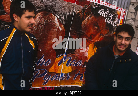 Deux jeunes hommes asiatiques britanniques se tenir en face d'un héros d'action Bollywood affiche, en attendant un bus à Southall. Banque D'Images