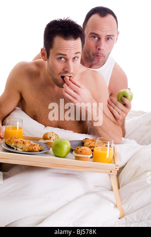 Un couple homo heureux et leur petit-déjeuner sur un plateau au lit Banque D'Images