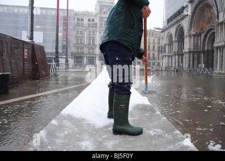 Un homme efface la neige des trottoirs dans une inondé la place Saint-Marc, Venise, Italie Banque D'Images