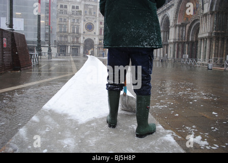 Un homme efface la neige des trottoirs dans une inondé la place Saint-Marc, Venise, Italie Banque D'Images