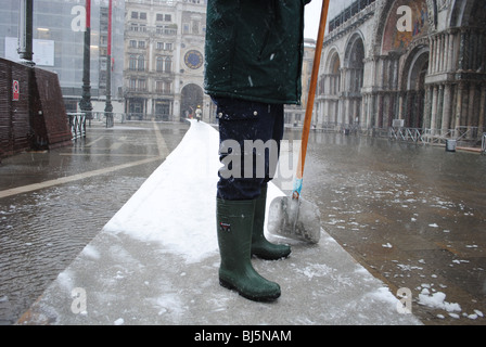 Un homme efface la neige des trottoirs dans une inondé la place Saint-Marc, Venise, Italie Banque D'Images