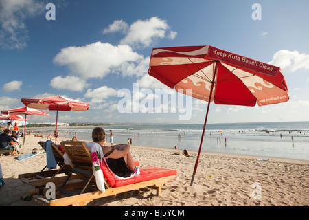 L'INDONÉSIE, Bali, Kuta, plage, femme assise sur une chaise longue à l'ombre de garder propre parasol de plage de Kuta Banque D'Images