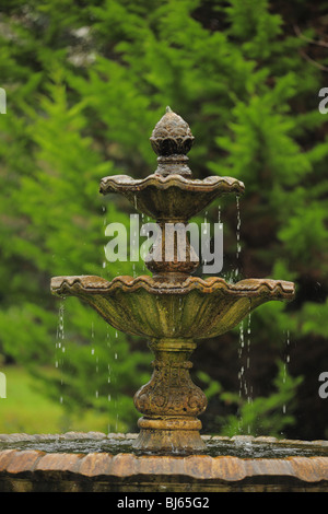 Fontaine à plusieurs niveaux avec de l'eau dégoulinant le long d'un bol à l'autre contre des arbres en arrière-plan Banque D'Images