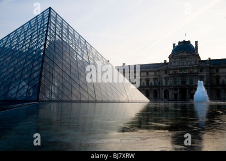 L'aube et le lever de soleil sur l'étang gelé d'hiver près de la pyramide de verre du Louvre Museum / Musée / Palais du Louvre. Paris, France. Banque D'Images