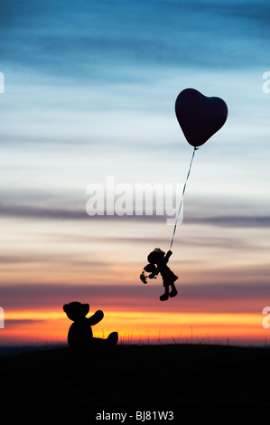 Poupée de chiffon holding sur un ballon d'hélium en forme de coeur s'envoler d'un ours au lever du soleil. UK. Still Life silhouette Banque D'Images