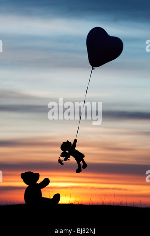 Poupée de chiffon holding sur un ballon d'hélium en forme de coeur s'envoler d'un ours au lever du soleil. UK. Still Life silhouette Banque D'Images