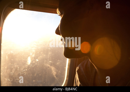 Jeune femme regardant par la fenêtre sur un avion, avec sun flare Banque D'Images