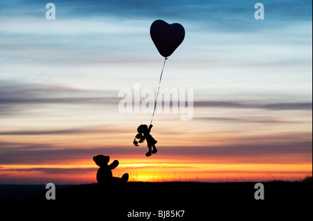 Poupée de chiffon holding sur un ballon d'hélium en forme de coeur s'envoler d'un ours au lever du soleil. UK. Still Life silhouette Banque D'Images