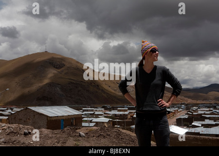 Femme occidentale dans un chapeau et des lunettes de soleil en face de village de montagne péruvienne Banque D'Images