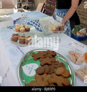 Femme vendant des gâteaux, muffins, cupcakes et gingerbread men at a cake stand at a market Banque D'Images