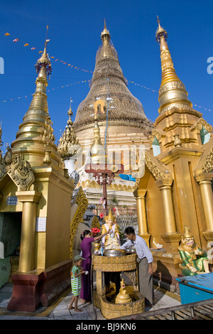 Famille birmane verser de l'eau sur une statue de Bouddha (rituel bouddhiste traditionnelle). Paya Shwedagon. Yangon. Myanmar Banque D'Images