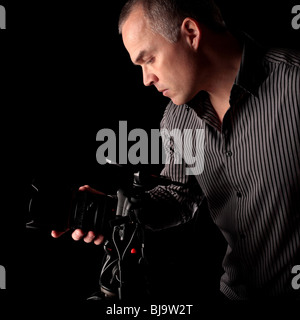 Homme d'âge moyen de prendre une photo avec un appareil photo reflex numérique dans le noir sur fond noir Banque D'Images