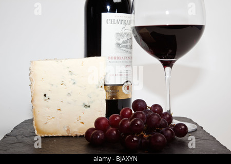 Still Life de vin rouge, un morceau de fromage bleu, raisin et une bouteille de vin rouge à l'ardoise noire sur un fond blanc Banque D'Images