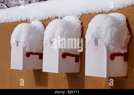 Trois boîtes aux lettres blanches intégrées dans Adobe mur recouvert de neige. Banque D'Images