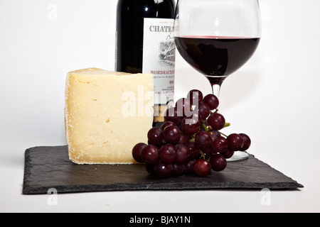 Still Life de vin rouge, un morceau de fromage, raisins et une bouteille de vin rouge sur une ardoise noire sur un fond blanc Banque D'Images