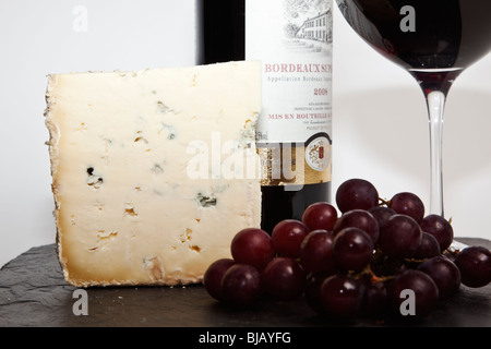 Still Life de vin rouge, un morceau de fromage bleu, raisin et une bouteille de vin rouge à l'ardoise noire sur un fond blanc Banque D'Images