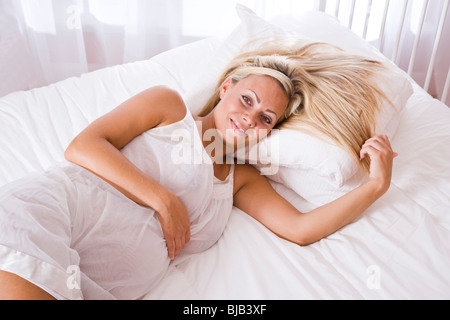 Jeune blonde pregnant woman lying down on bed Banque D'Images