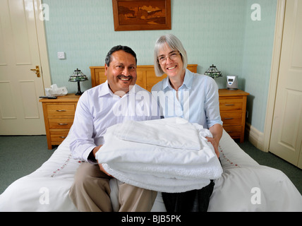 Un couple en marche un bed and breakfast guesthouse assis sur un lit avec des draps vous UK Banque D'Images