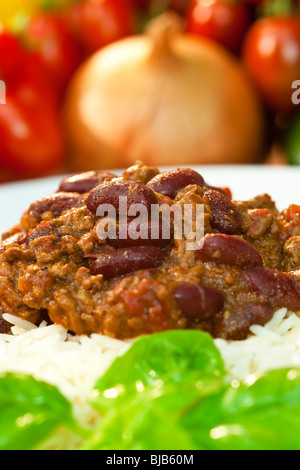 Chili con Carne sur le riz blanc et garnir de basilic avec les oignons et les tomates non mise au point à l'arrière-plan Banque D'Images