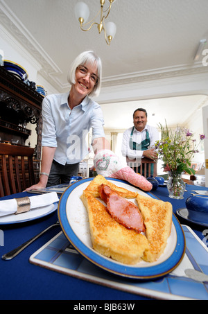 Un couple en marche un bed and breakfast guesthouse sert le petit-déjeuner de pain doré et du bacon pour un invité Banque D'Images