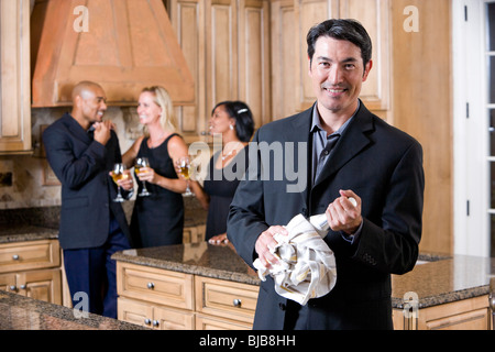 Homme avec bouteille de champagne dans la cuisine, groupe d'amis, bavarder en arrière-plan Banque D'Images