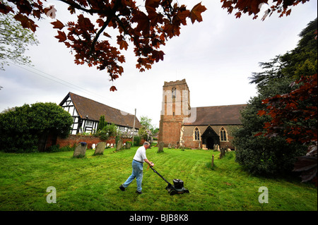 Un homme tond le gazon dans le cimetière à l'église de St Bartholomew's dans le village d'Redmarley Abitot D', Gloucestershire Banque D'Images