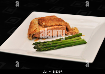 Saumon en croute aux asperges vertes sur une assiette blanche sur noir table cloth Banque D'Images