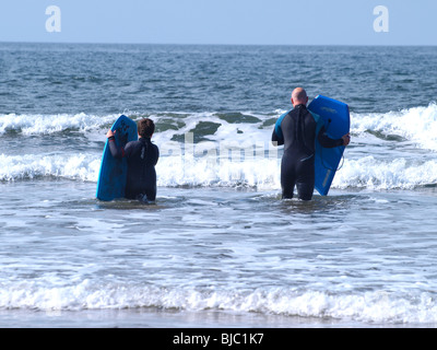 Père et fils avec bodyboards aller dans la mer, Cornwall Banque D'Images