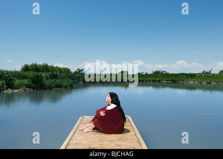 Femme assise sur un quai d'une couverture enroulée autour d'elle, les yeux fermés Banque D'Images