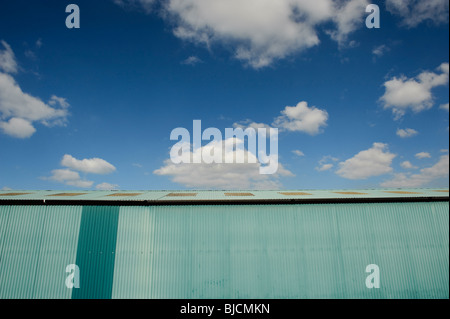 Hangar en tôle ondulée peinte en bleu, avec ciel bleu et nuages blancs Banque D'Images