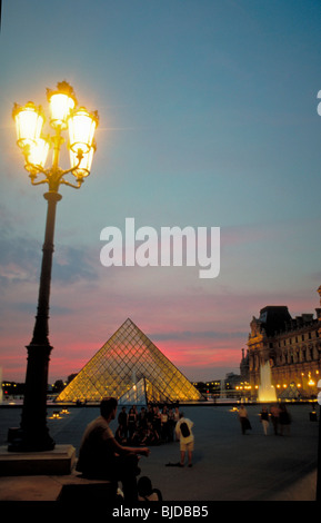 Paris, France- touriste masculin regardant la pyramide de verre au Musée du Louvre, illuminé au crépuscule, vieux lampadaire de paris Banque D'Images