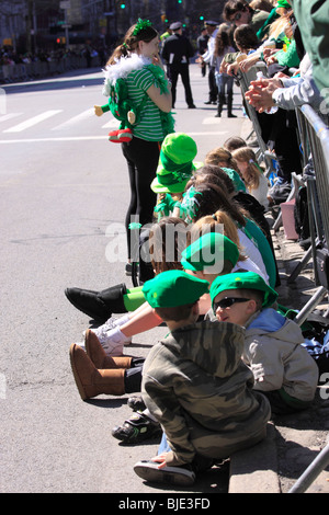 Des enfants assis sur le trottoir à regarder le défilé de la Saint-Patrick, la 5e Avenue, New York City Banque D'Images