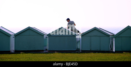 Man painting cabanes de plage le long du front de mer sur une chaude Hove matin ensoleillé UK Banque D'Images