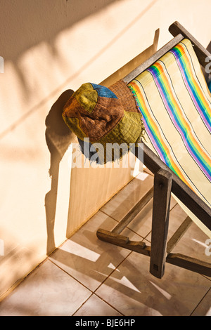 Locations de paresseux dans le soleil avec un chapeau tropical bohème suspendus sur une chaise pliable sur le porche d'un bungalow plage. Banque D'Images