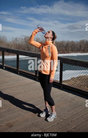 Femme buvant de l'eau après une course par un beau jour d'hiver Banque D'Images