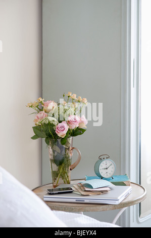 Roses dans un vase sur la table de chevet avec livres et réveil Banque D'Images