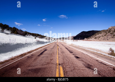 Une route mène au loin dans les montagnes enneigées. Banque D'Images