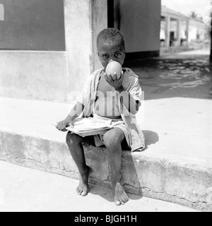 L'Afrique, 1950. Photographie par J Allan Paiement d'un jeune garçon, pieds nus du Mozambique Assis sur un trottoir. Banque D'Images