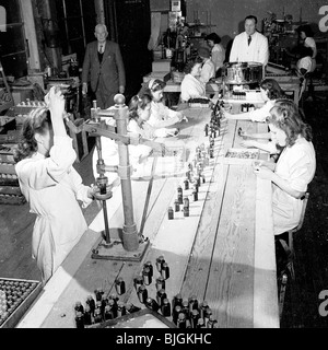 Angleterre, années 1950. Groupe des travailleurs féminins sur une ligne de production mise sur les couvercles des bouteilles de comprimés, contrôlé par les hommes de superviseurs. Banque D'Images