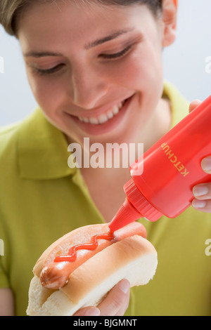 Jeune femme de mettre du ketchup sur hot dog - Banque D'Images