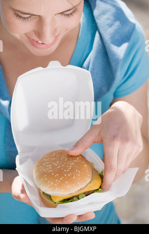 Jeune femme prenant cheeseburger hors de boîte en polystyrène - Banque D'Images