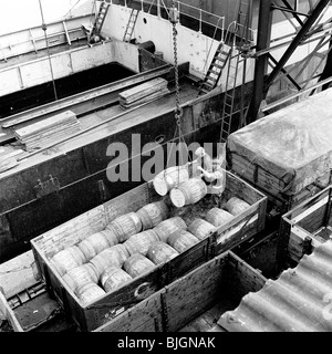 Docks de Londres, 1950 Deux travailleurs superviser barils d'être chargé d'un navire, tenir sur un camion rail GWR sur les voies latérales. Banque D'Images