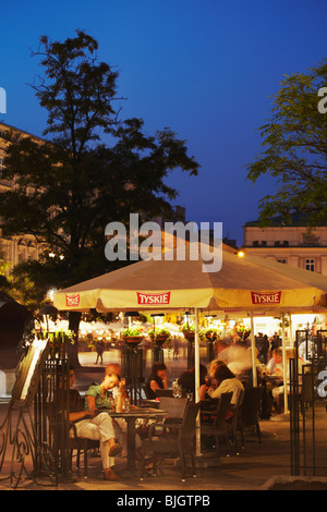 Dans les cafés en plein air place du marché (Rynek Glowny) au crépuscule, Cracovie, Pologne Banque D'Images